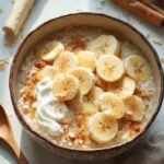 "Overhead shot of banana oat power bowl with sliced bananas, Greek yogurt and cinnamon on white marble surface"