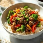"Overhead shot of a budget pork stir-fry with ground pork, colorful vegetables, rice and toasted sesame seeds on a clean marble countertop."