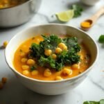 "Overhead shot of chickpea coconut curry with wilted kale on a clean marble background, with key ingredients scattered around."