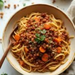 "Bowl of lentil bolognese pasta with fresh herbs on clean marble surface"