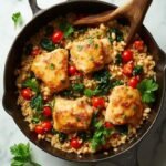 "Overhead view of a Mediterranean Bean and Rice Bowl with chunks of chicken thigh, cannellini beans, brown rice, diced tomatoes, and spinach in a rustic Dutch oven on a clean white marble surface."