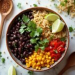 "Overhead shot of a budget-friendly high-fiber weight loss bowl with brown rice, black beans, corn, and red bell peppers, garnished with cilantro, served on a white marble surface."