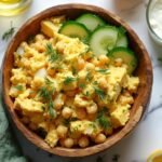 "Overhead shot of chunky chickpea and egg salad in a rustic bowl, surrounded by ingredients, on a clean white background."