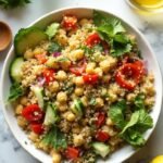 "High protein chickpea and quinoa salad with fresh vegetables and lemon dressing in a white ceramic bowl on a marble countertop"