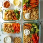 "High protein budget meal prep bowls filled with quinoa, chicken, roasted vegetables, chickpeas, and Greek yogurt, arranged on clean marble countertop with raw ingredients scattered around"
