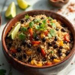 "Overhead shot of high protein rice and beans with black beans, brown rice, bell peppers, cilantro, and lime garnish on a clean white marble background."