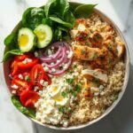 "Mediterranean rice bowl with grilled chicken, feta cheese, fresh vegetables, hummus, and tzatziki on a clean white background"