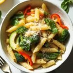 "One-pot pasta primavera with spring vegetables and Parmesan cheese in a white bowl on a clean marble background"