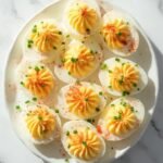"Overhead shot of twelve deviled eggs with paprika and chives on a clean marble background"