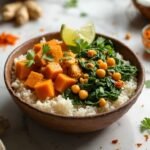 "Sweet potato curry with chickpeas, spinach, coconut milk and rice in a rustic ceramic bowl, garnished with cilantro on a white marble countertop."