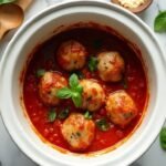 "Slow cooker turkey meatballs in marinara sauce with fresh basil garnish on a clean marble countertop"