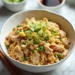 "Overhead shot of turkey mince fried rice with scrambled eggs, peas, and spring onions in a white bowl, with soy sauce and sesame oil in the background"