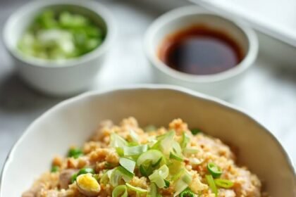 "Overhead shot of turkey mince fried rice with scrambled eggs, peas, and spring onions in a white bowl, with soy sauce and sesame oil in the background"